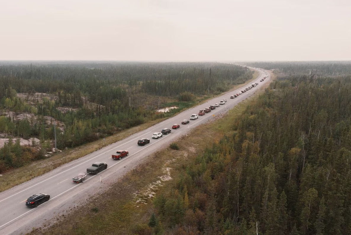 Photo of cars lined up into the distance fleeing the Yellowknife fire in Canada, sky thck with smoke haze.